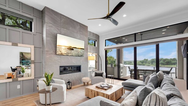 A modern living room with a fireplace, large windows, a ceiling fan, and a view of the outdoors. - The Escape at 212 | Concierge Services | Promos Available (Burnet)
