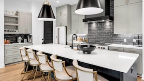 A modern kitchen with a central island, bar stools, pendant lights, and a black stove. - The Escape at 212 | Concierge Services | Promos Available (Burnet)