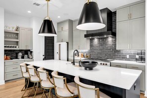 A modern kitchen with a central island, bar stools, pendant lights, and a black stove. - The Escape at 212 | Concierge Services | Promos Available (Burnet)
