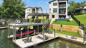A modern multi-story building with a dock extending into a body of water, equipped with lounge chairs and a covered area. - The Escape at 212 | Concierge Services | Promos Available (Burnet)