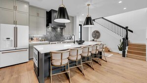 A modern kitchen with a central island, bar stools, a staircase, and a dining area. - The Escape at 212 | Concierge Services | Promos Available (Burnet)