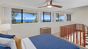 A bedroom with a bed, a nightstand, a wooden crib, and large windows offering a view of the ocean.