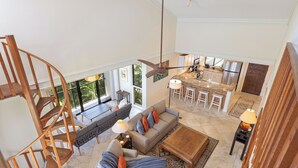 A spacious living area with a sofa, coffee table, and a spiral staircase. A kitchen with a bar and large windows is visible in the background.