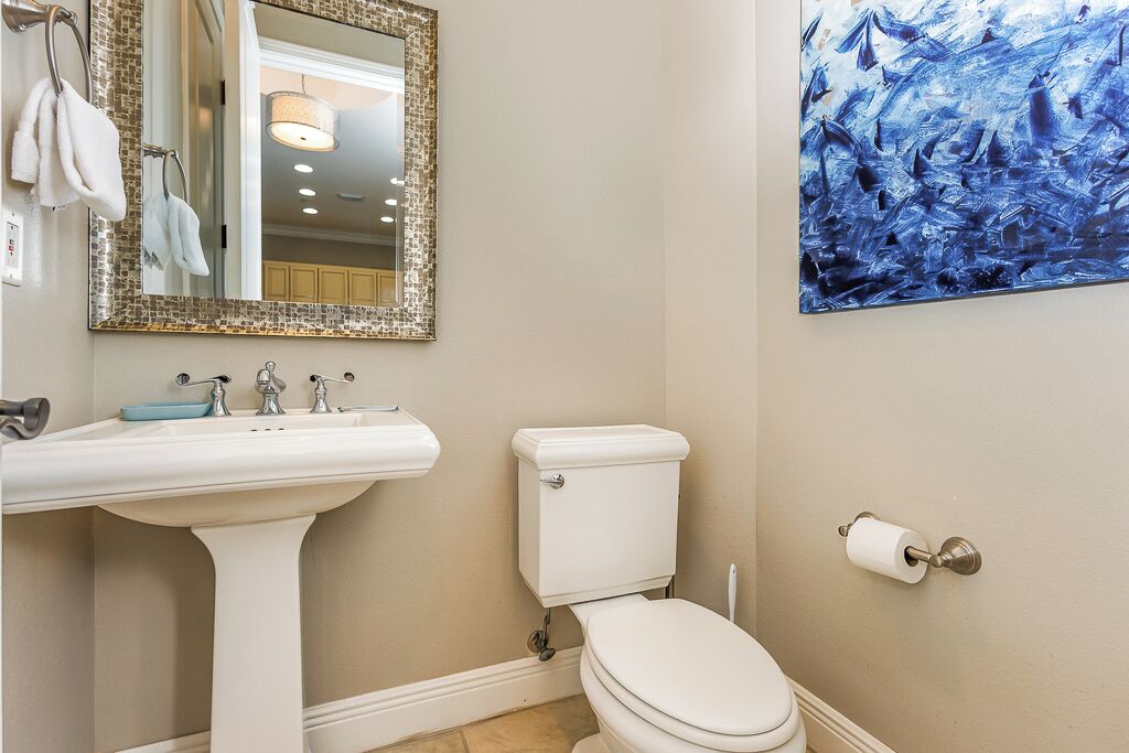 A bathroom with a white sink, a toilet, a mirror with a decorative frame, and a blue abstract painting on the wall.