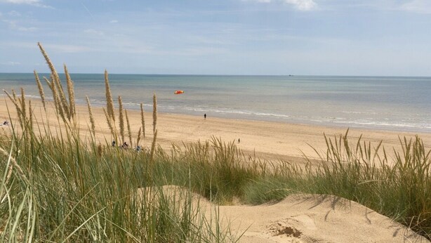 A beach with sand dunes and grass in the foreground, a clear sky, and calm water. - Happy Waves - Family House - 1 Min to Camber Sands (Camber)