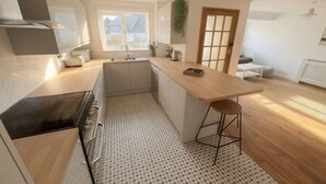 A modern kitchen with a central island, a built-in oven, and a window overlooking a residential area. - Happy Waves - Family House - 1 Min to Camber Sands (Camber)