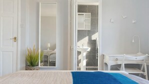 A bedroom with a bed, a bedside table, a mirror, a wardrobe, and a bathroom with a sink and shower. - Happy Waves - Family House - 1 Min to Camber Sands (Camber)