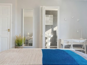 Une chambre Ă coucher comprenant un lit, une table de chevet, un miroir, une armoire, ainsi quâune salle de bain avec un lavabo et une douche.
