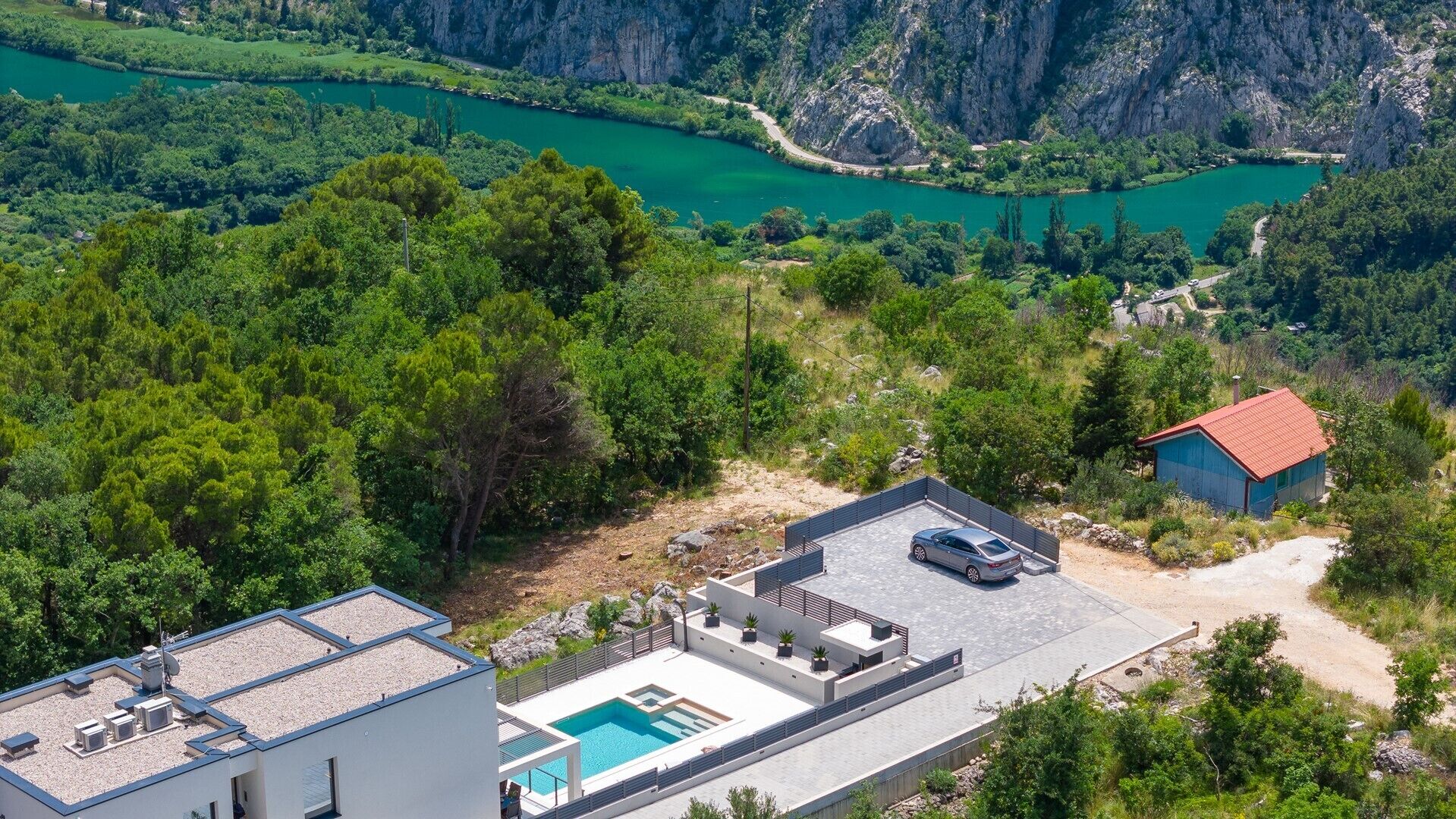 Ein modernes Gebäude mit Pool auf dem Dach, umgeben von üppiger Vegetation und Blick auf einen Fluss.