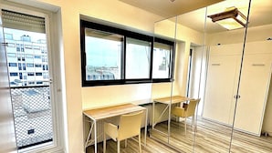 Une pièce avec une grande fenêtre, un bureau, une chaise et une armoire.