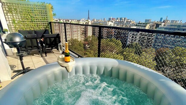 Un bain à remous avec une bouteille de champagne sur un balcon donnant sur une vue panoramique de la ville.