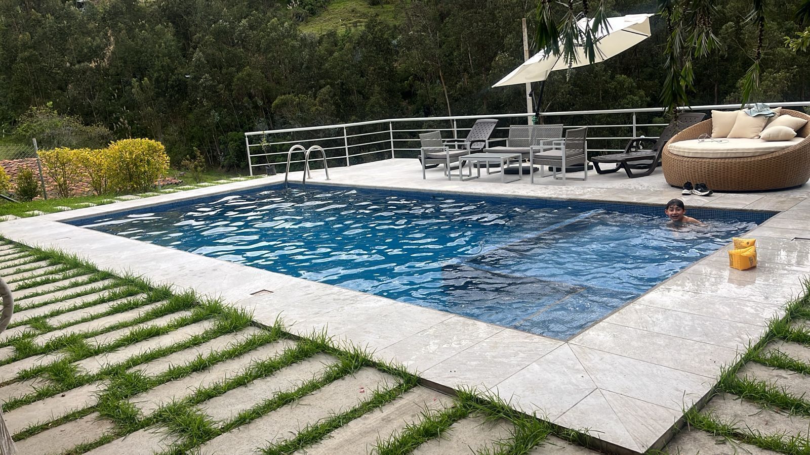 A swimming pool with a surrounding deck, lounge chairs, and a grassy area.