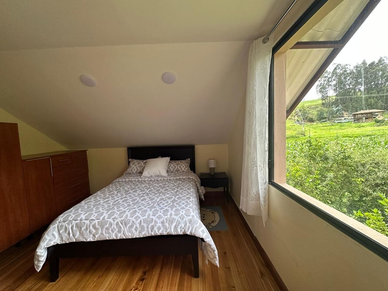Un dormitorio con cama, mesita de noche, armario y ventana con vistas a la vegetación.