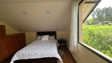 A bedroom with a bed, a nightstand, a wardrobe, and a window with a view of greenery.