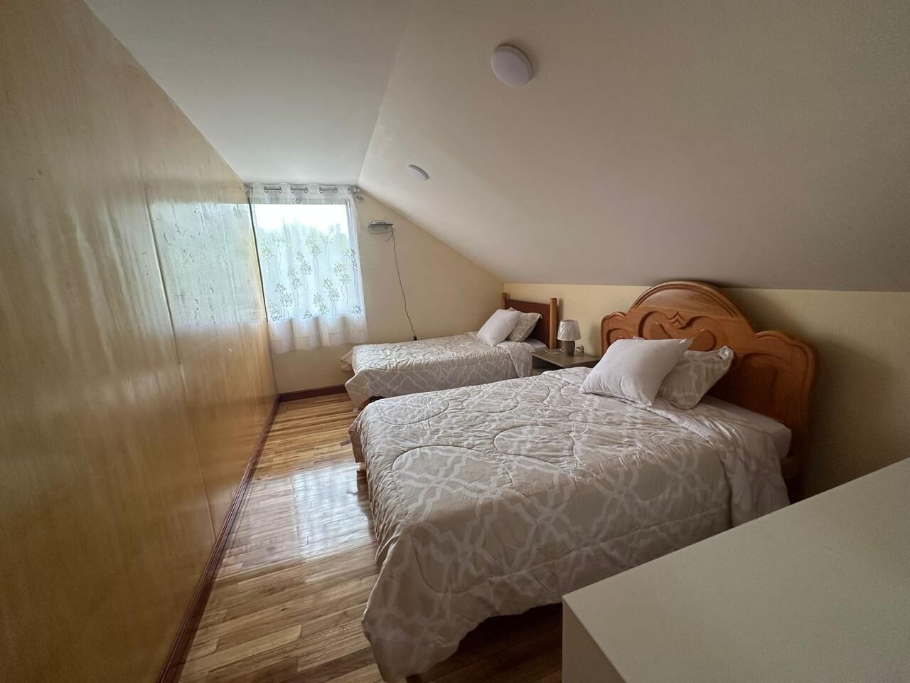 A small, cozy room with two single beds, a wooden floor, and a sloped ceiling.