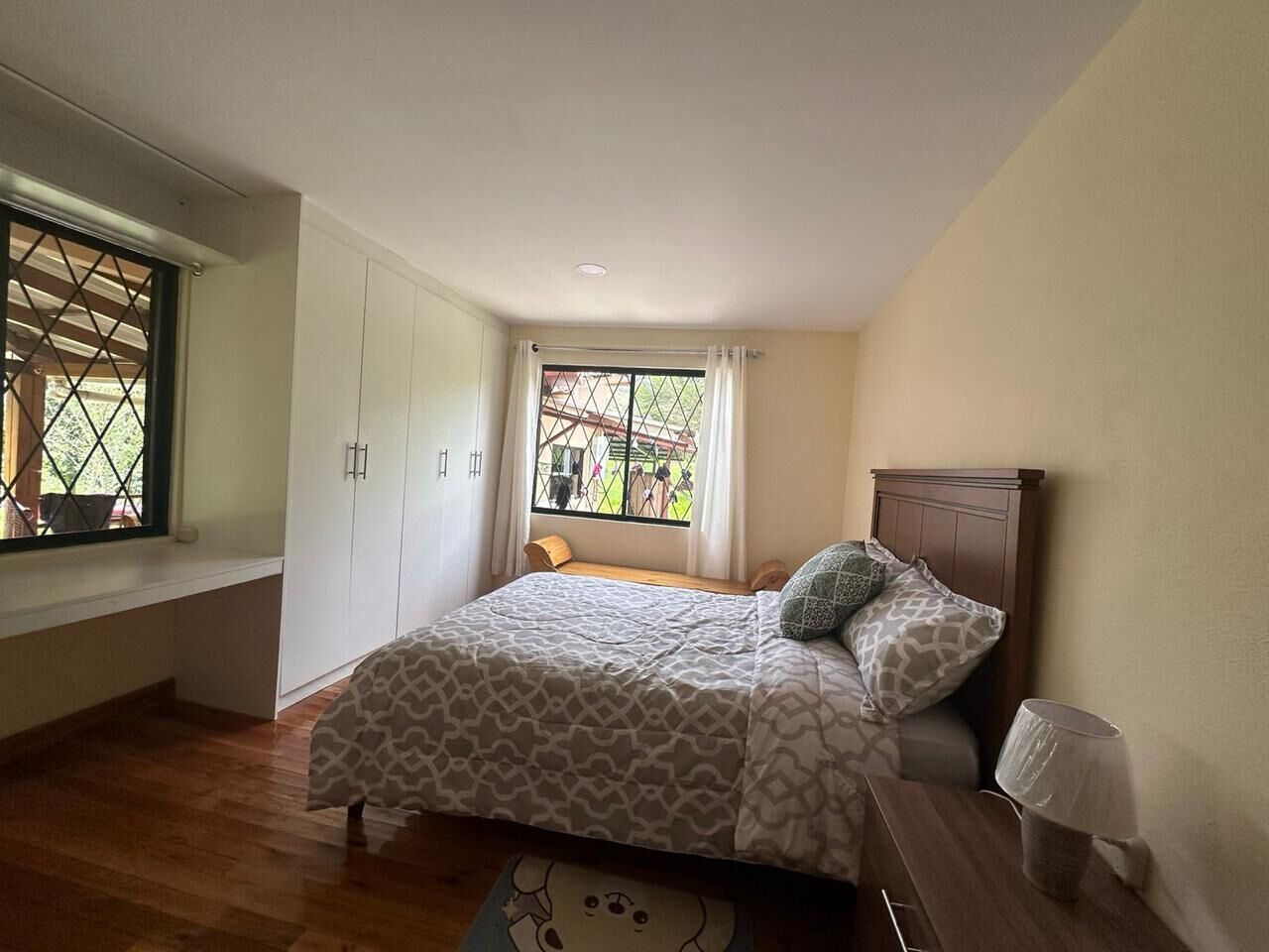 A bedroom with a bed, a window, a wooden bench, and a lamp.