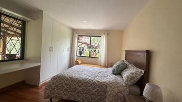 A bedroom with a bed, a window, a wooden bench, and a lamp.