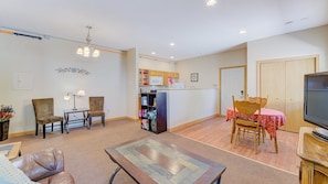 Ein Wohnzimmer mit Sofa, zwei Sessel, einem Couchtisch, einem Fernseher und einer Küchenzeile mit Schränken und einem Kühlschrank.