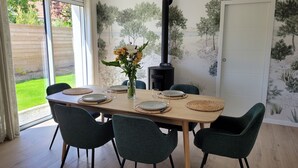 A dining area with a table set for four, a vase with flowers, and a wood-burning stove. - Maison de Vacances à 2 pas de la Plage et des Commerces (Pornic)
