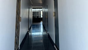 Egy hosszú, keskeny folyosó, fehér falakkal és sötét színű, csempézett padlóval. Mindkét oldalon vannak ajtók, az egyiken mintás, a másikon pedig egyszerű, egyszínű ajtó található.