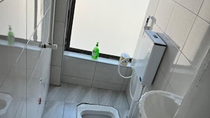 Egy kis, modern fürőszoba, amelyben WC, bidé és egy ablak található.
