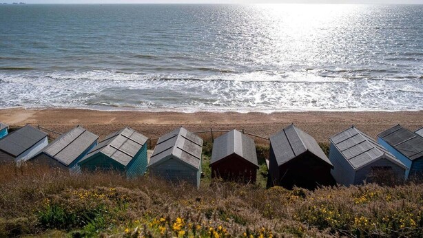 A beach with a row of beach huts and the ocean in the background. - Newgate Cottage by NewFo rest (Lymington)