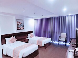 A hotel room with two beds, a desk with a computer, a chair, and a large window with curtains.