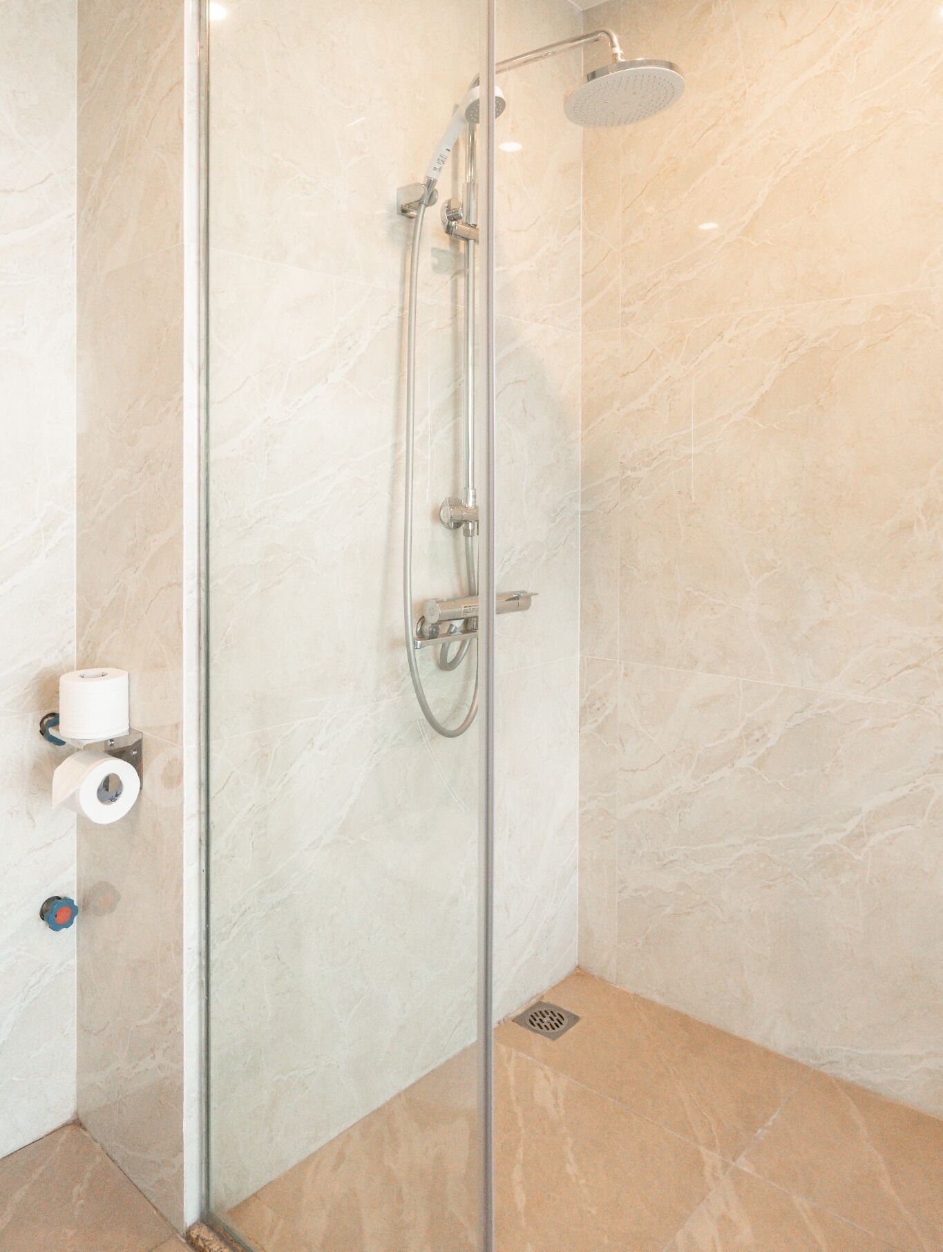 A glass-enclosed shower with a handheld showerhead and a wall-mounted control panel.