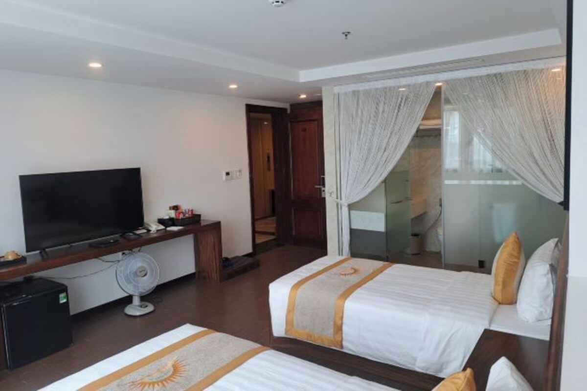 A hotel room with two beds, a TV, a fan, and a small desk.