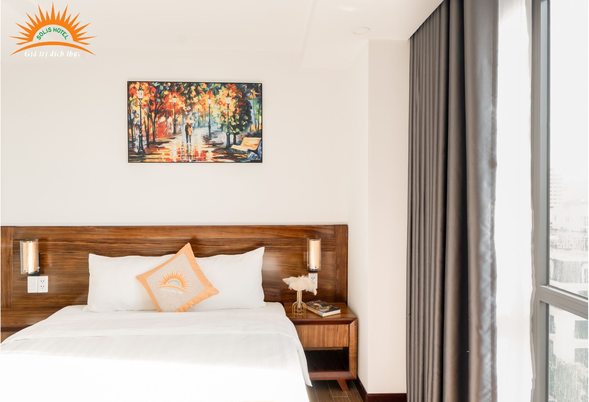 A hotel room with a wooden headboard, a painting of a park scene, a nightstand with a lamp, and a window with curtains.