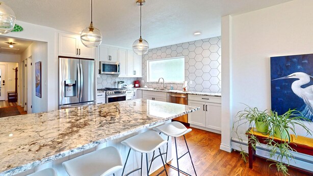 A modern kitchen with a marble countertop, stainless steel appliances, and a large window.