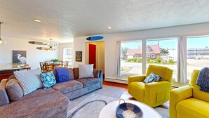 A spacious living room with a gray sofa, a yellow armchair, and a dining area with a red door.