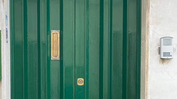 Puerta verde doble con dos pomos de bronce y un panel rectangular en el centro.