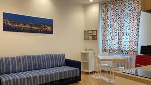 Una sala moderna con un sofá azul a rayas, piso de madera con un diseño de estrellas, un cuadro de un paisaje urbano, una cortina estampada y un mueble rojo.