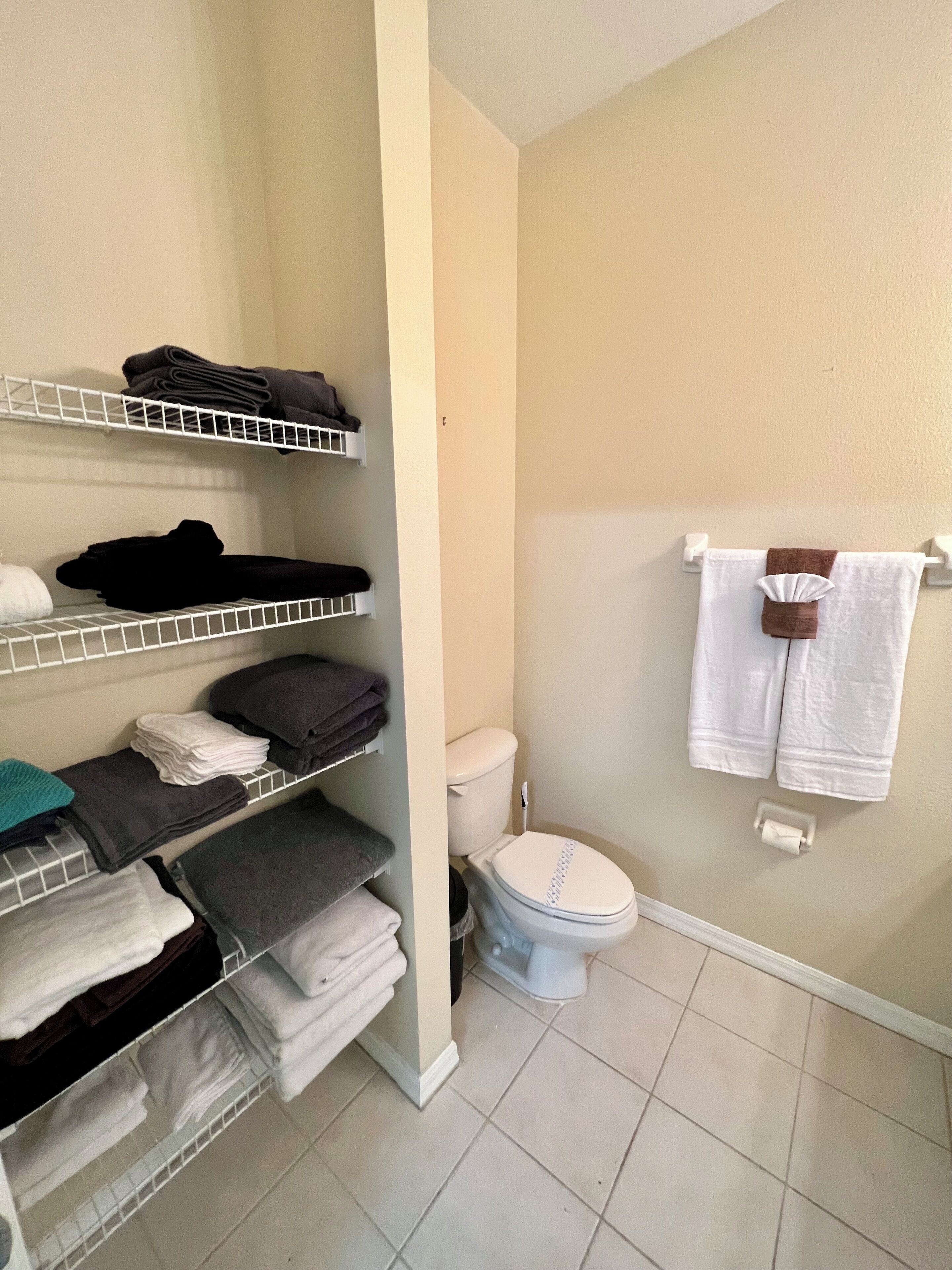 A bathroom with a toilet, a shelf with folded towels, and a towel rack with two towels.