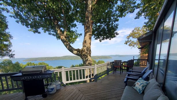 A wooden deck with a grill, outdoor furniture, and a view of a lake.