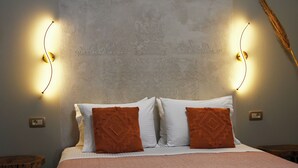 A neatly made bed with white and brown pillows, a pink blanket, and two wall-mounted light fixtures on either side. - Vivis Hub (Kefalonia)