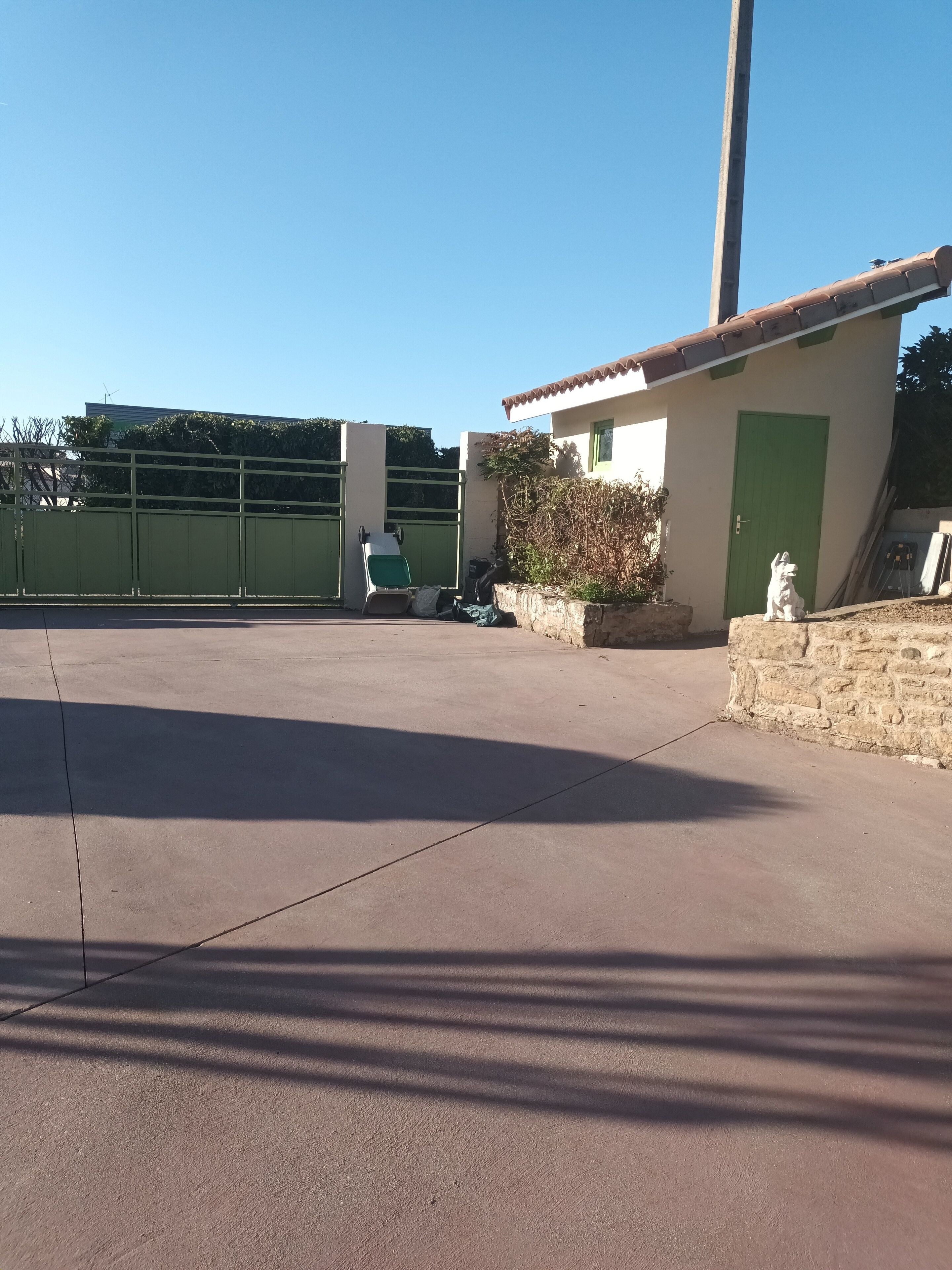 A concrete patio area with a green gate, a small building with a green door, and a statue of a dog.