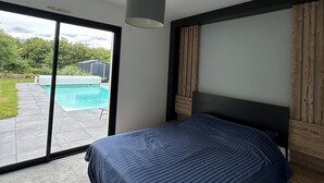 Un dormitorio con cama, luz en el techo, vista a una piscina y cabecera de madera.