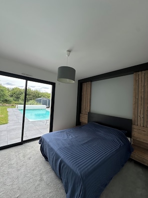 Un dormitorio con cama, luz en el techo, vista a una piscina y cabecera de madera.