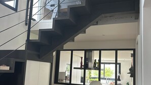 Un interior de varios niveles con una escalera, un sofá, una estantería y vistas al exterior.