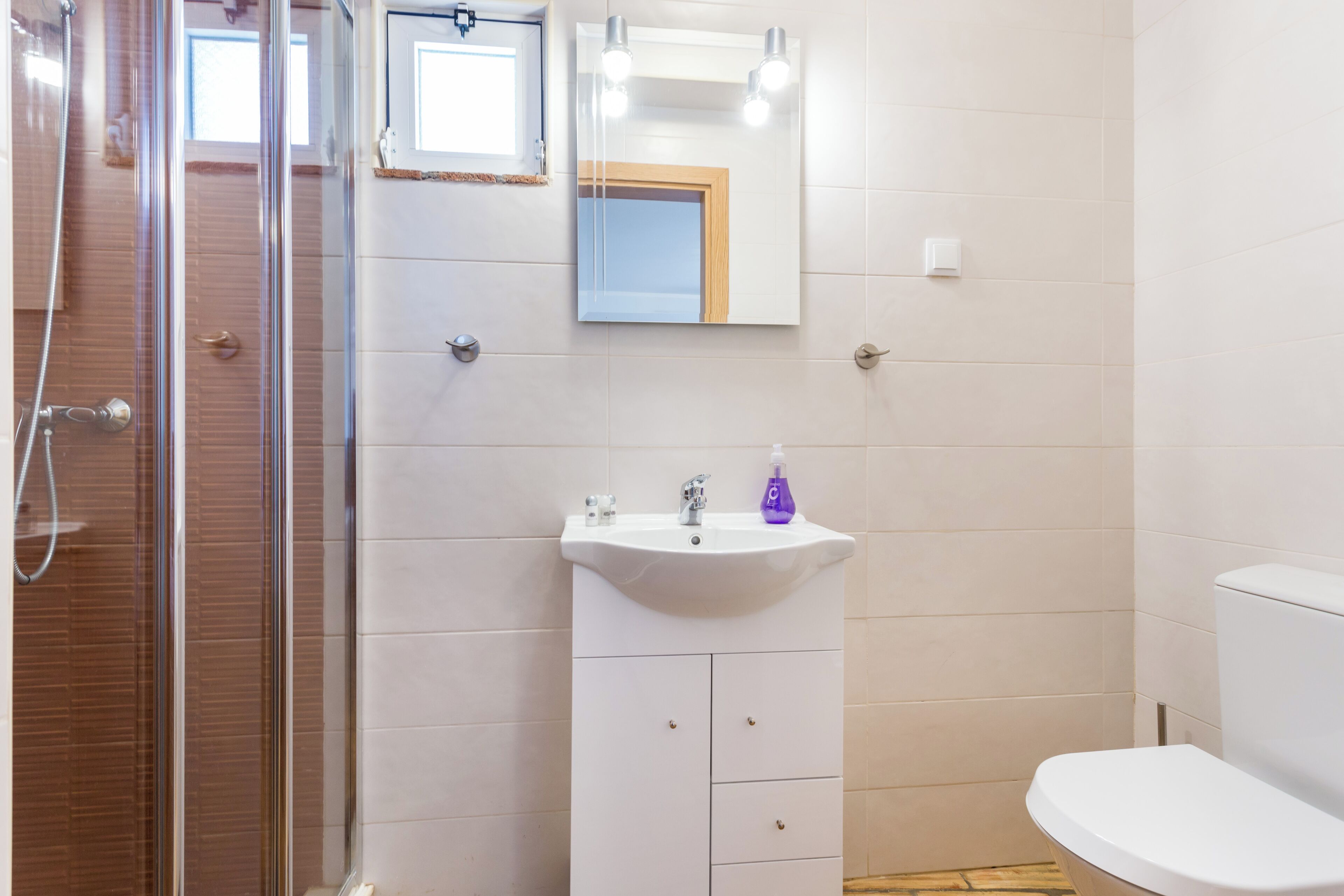 A bathroom with a shower, sink, toilet, and a mirror with lights.
