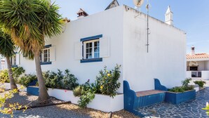 A white building with blue trim and shutters, surrounded by a garden with various plants and a palm tree. - Monte da Eirinha (Mertola)