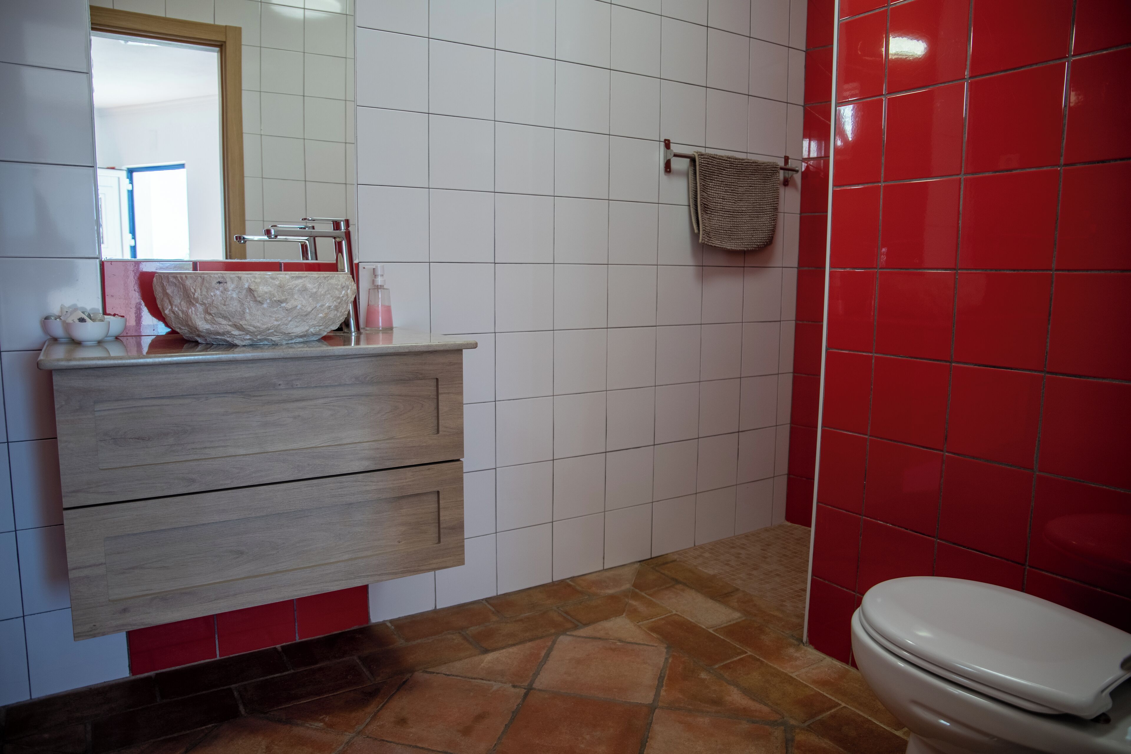Een badkamer met een wit wastafel, houten wastafelmeubel, rode betegelde wanden en een wit toilet.