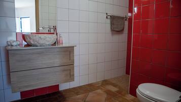 Een badkamer met een wit wastafel, houten wastafelmeubel, rode betegelde wanden en een wit toilet.