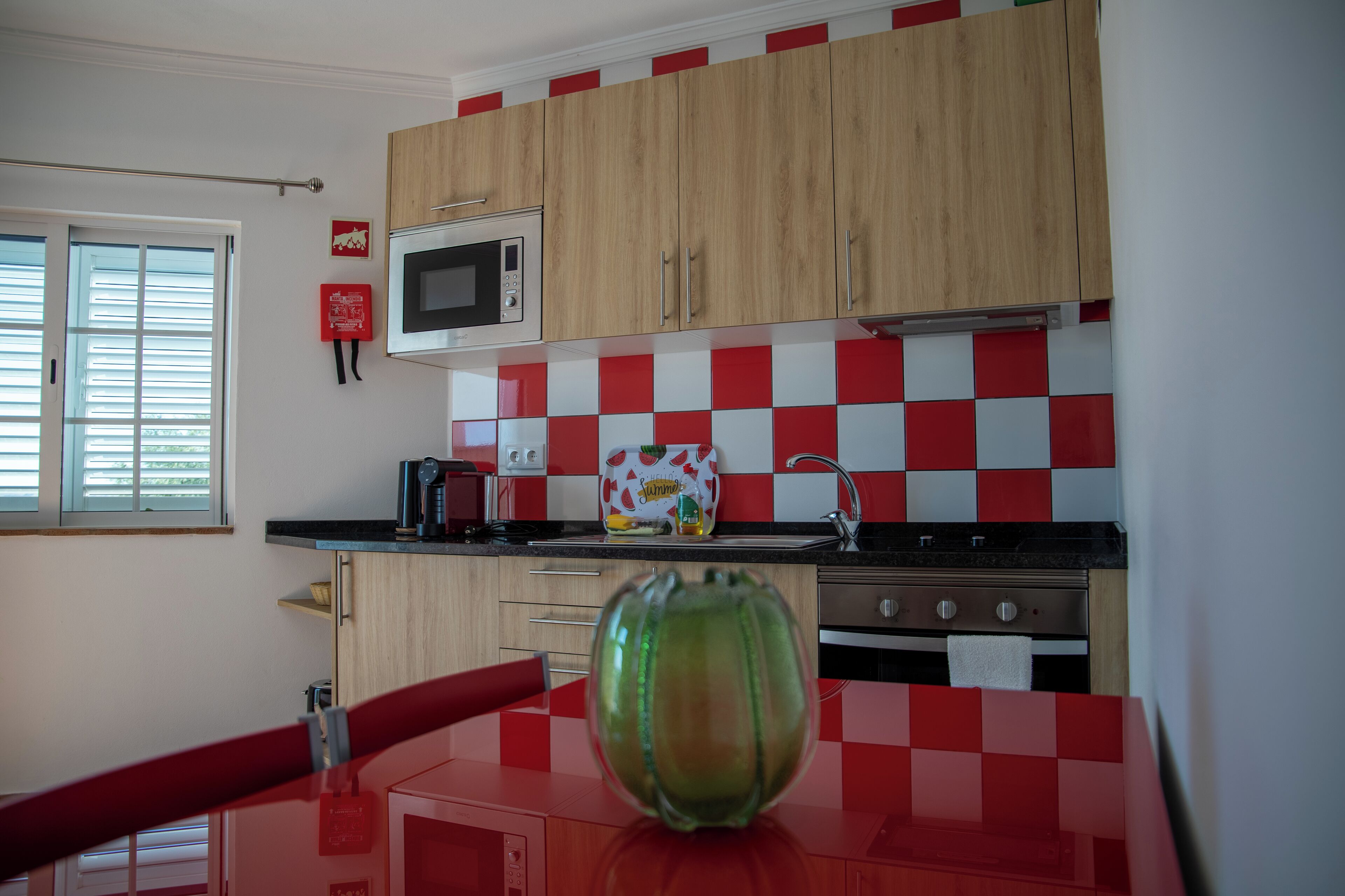 Una cocina con armarios de madera, microondas, fregadero y salpicadero a cuadros rojo y blanco.