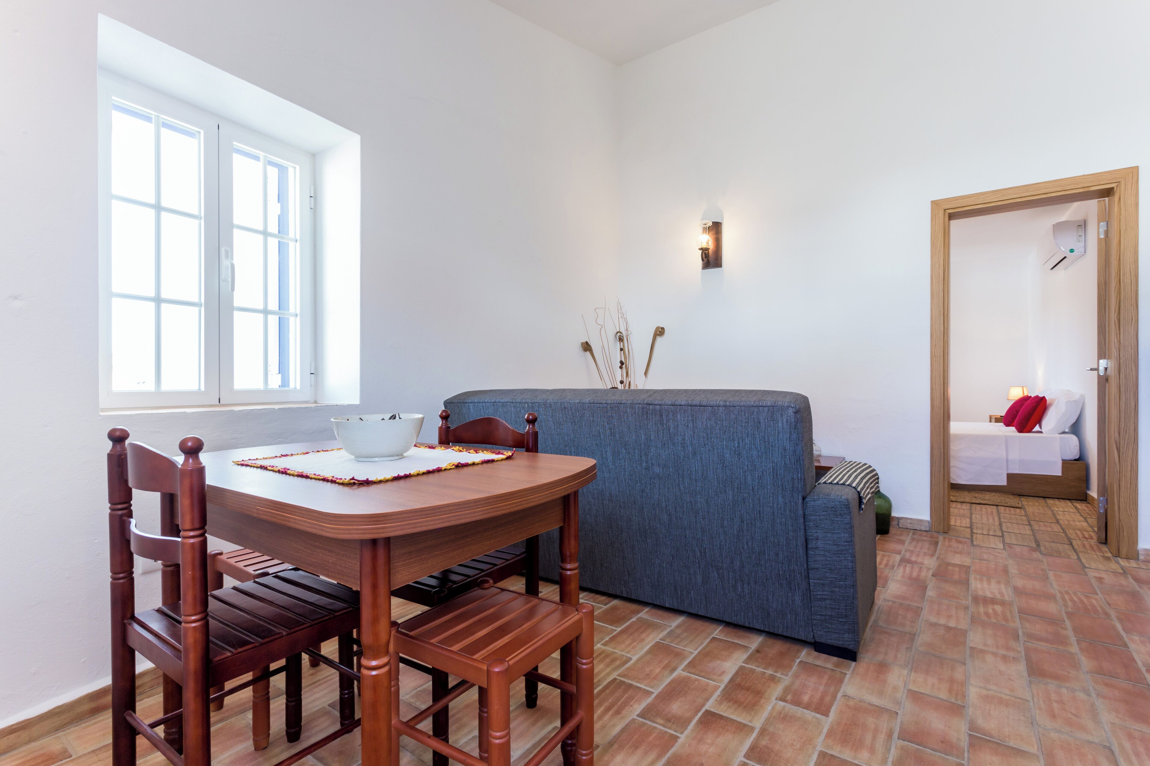 Ein Essbereich mit Holztisch und -stühlen, einem blauen Sofa und einem kleinen Fenster.
