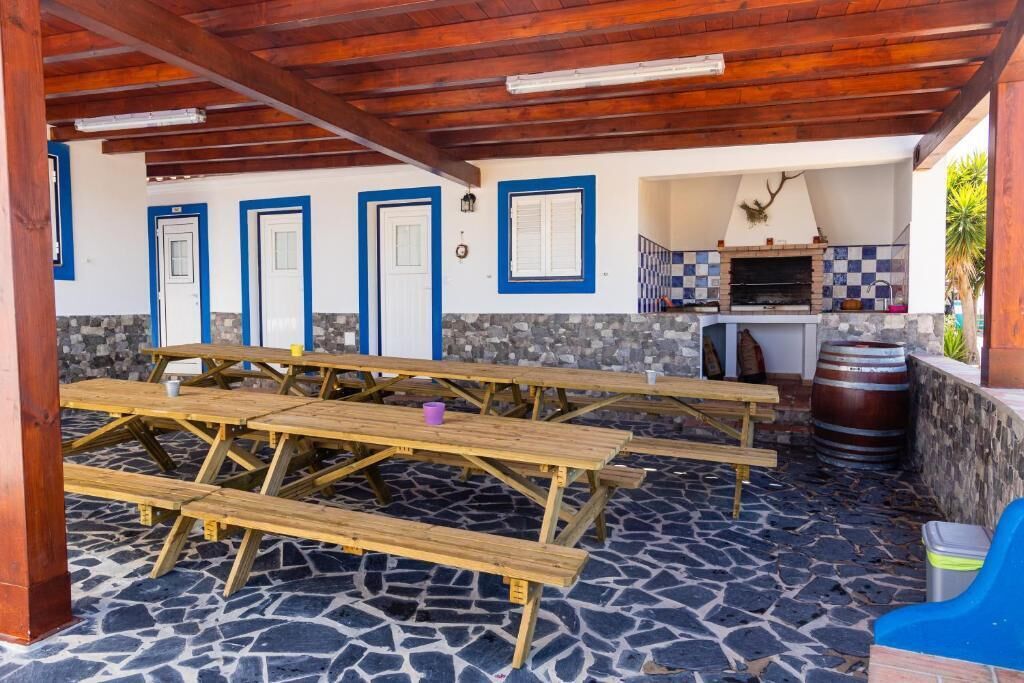 Une terrasse extérieure avec un sol en pierre, des tables de pique-nique en bois et un espace barbecue.