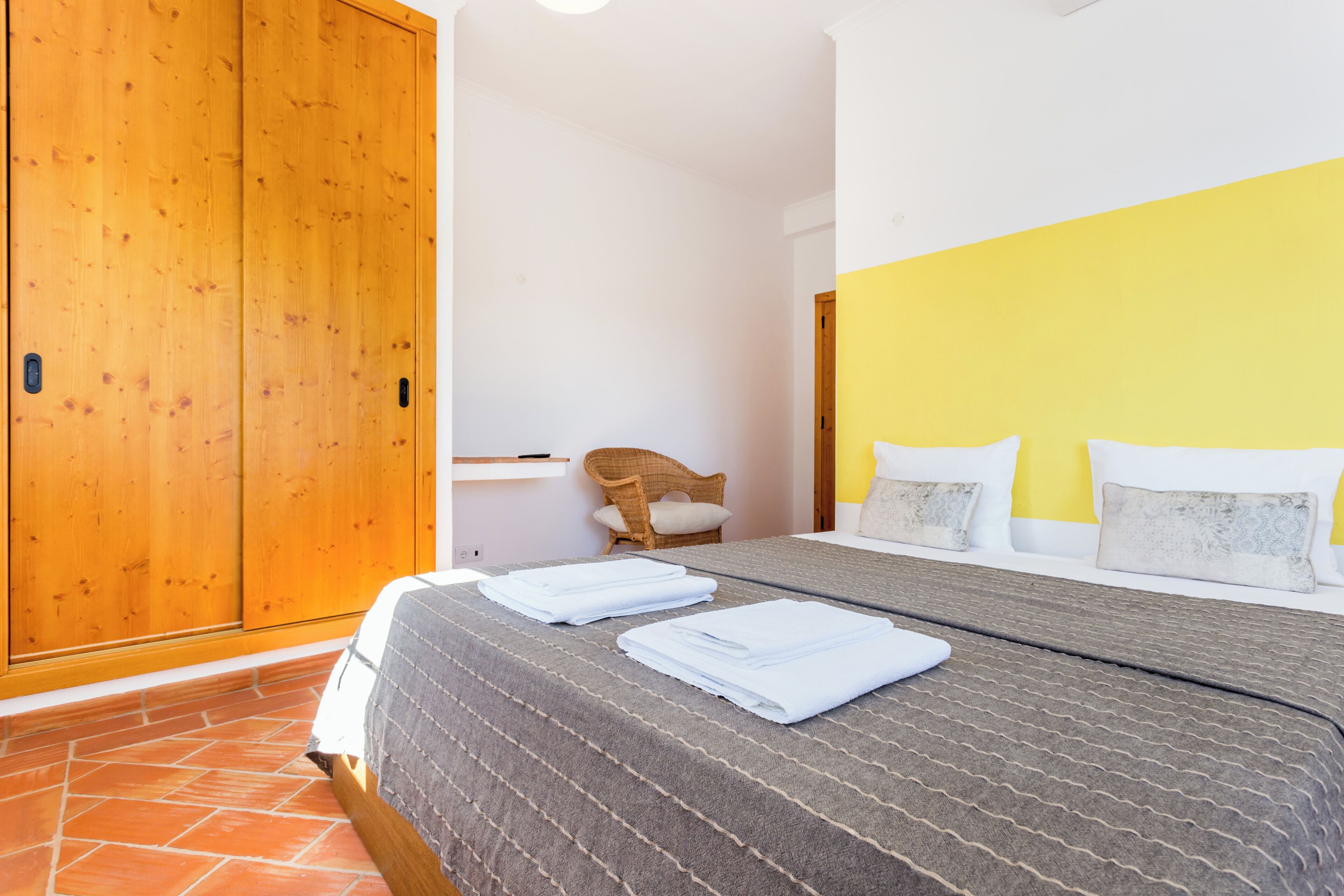 A bedroom with a bed, a wooden wardrobe, a chair, and a bedside table.