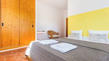A bedroom with a bed, a wooden wardrobe, a chair, and a bedside table.